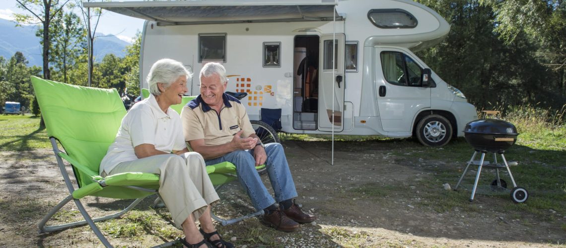 Senior couple sitting in front of camper van and having fun